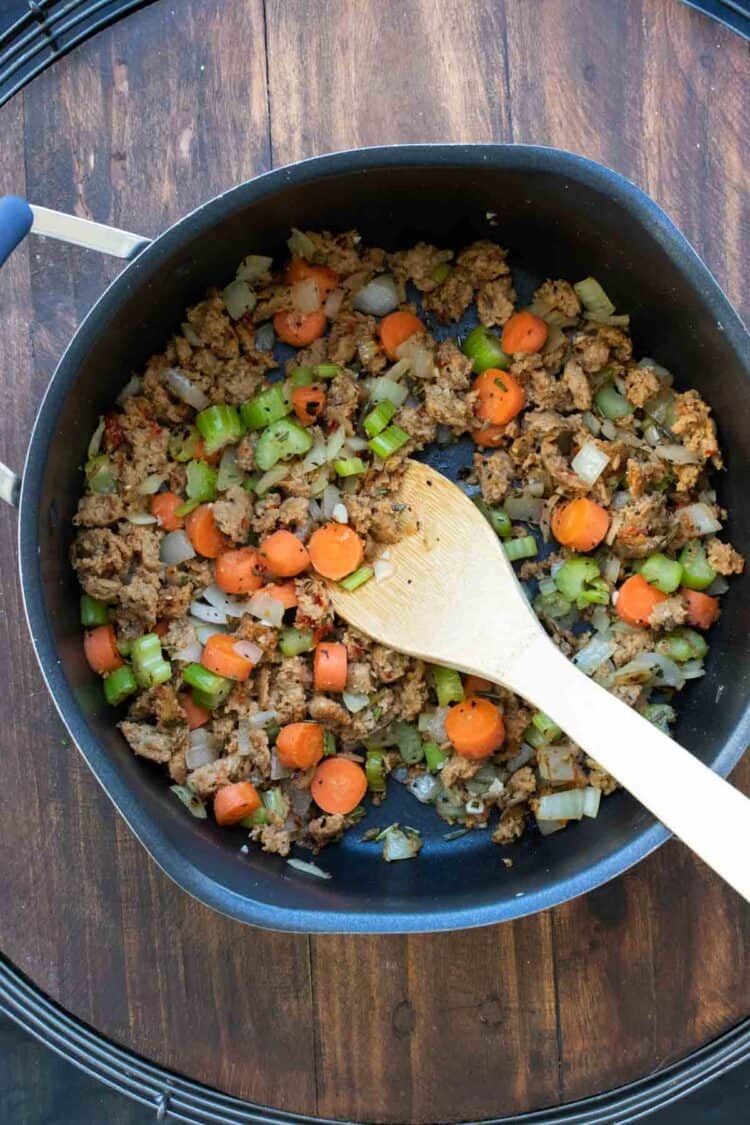 Sausage and vegetables being mixed in a pot by a wooden spoon.