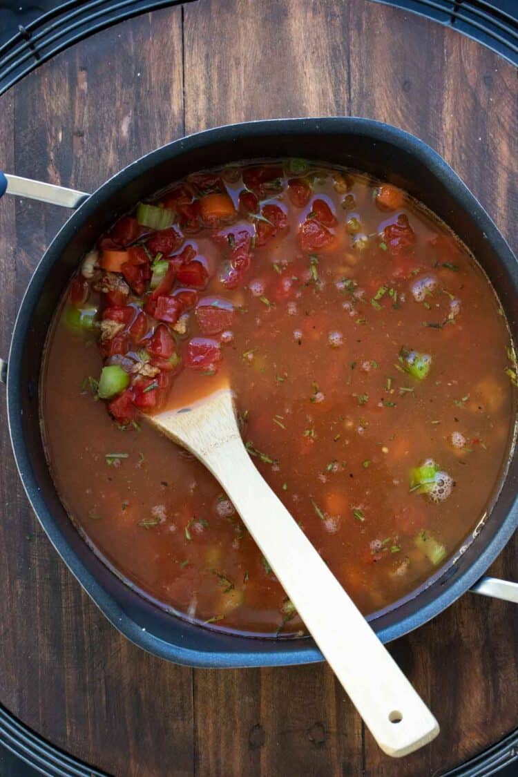 Wooden spoon mixing vegetable soup in a pot.