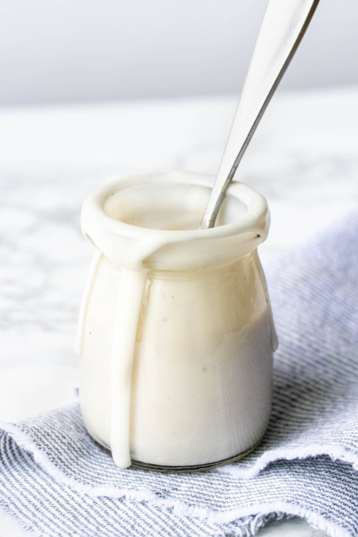 Glass jar with walnut cashew cream sauce dripping down the side.