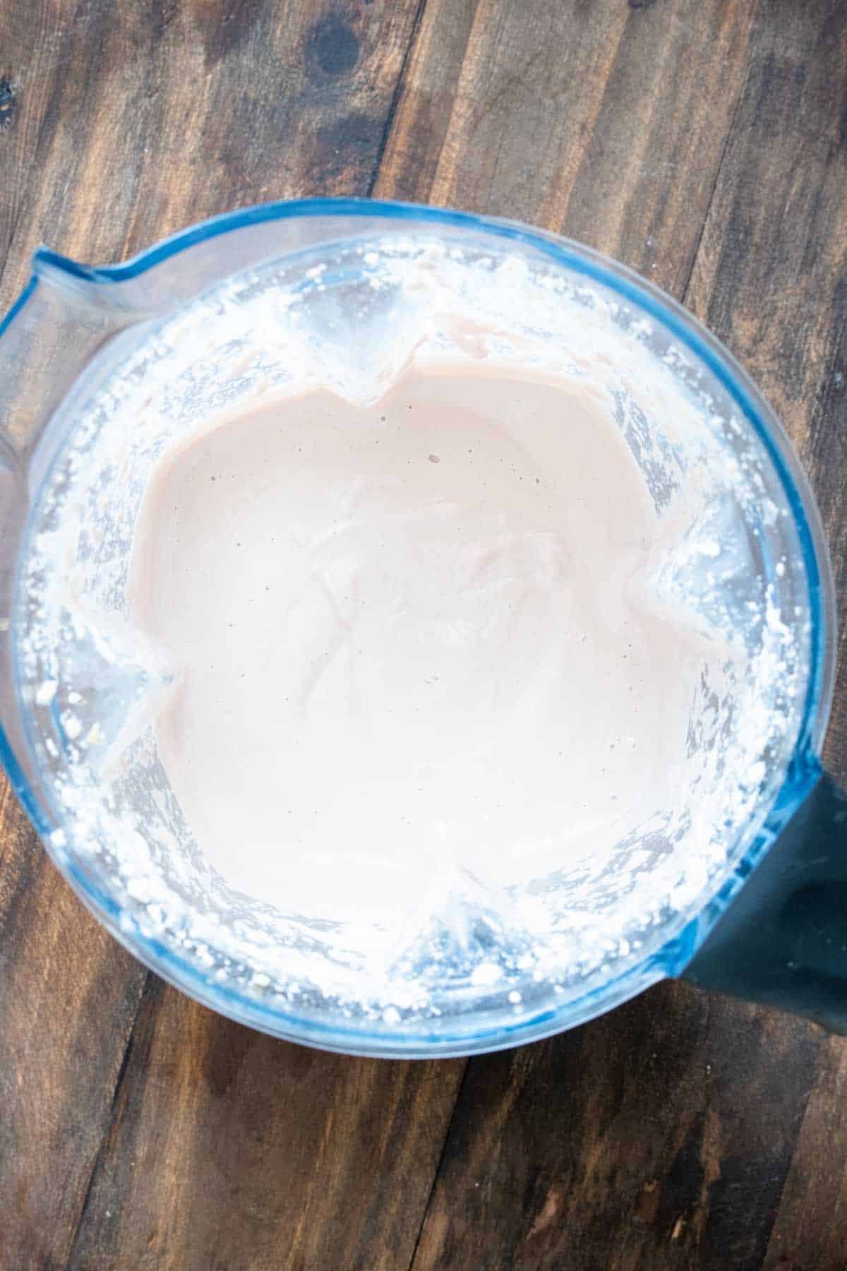 Top view of a blender sitting on a wooden surface with a cashew cream sauce inside.