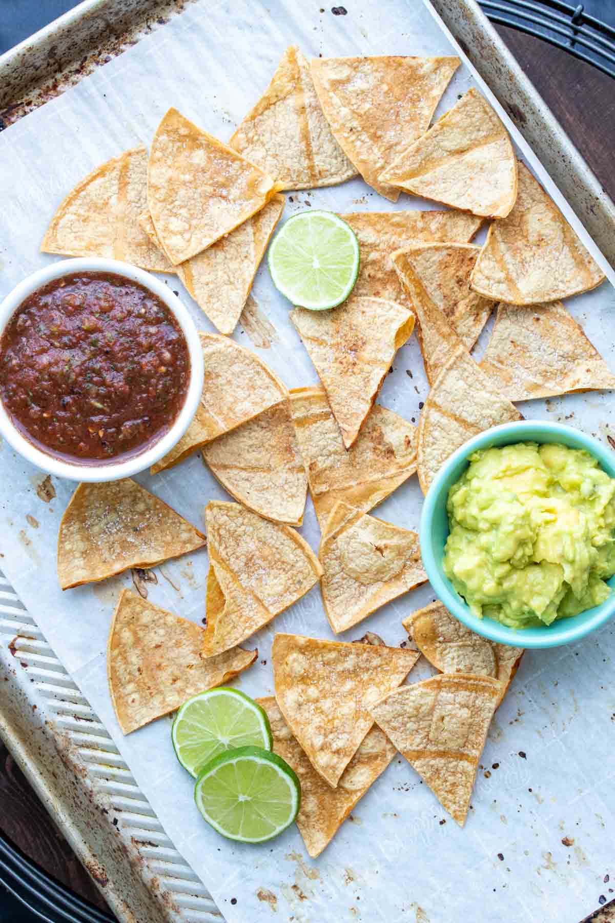 Parchment lined cookie sheet with bakes corn tortilla chips, salsa and guacamole.