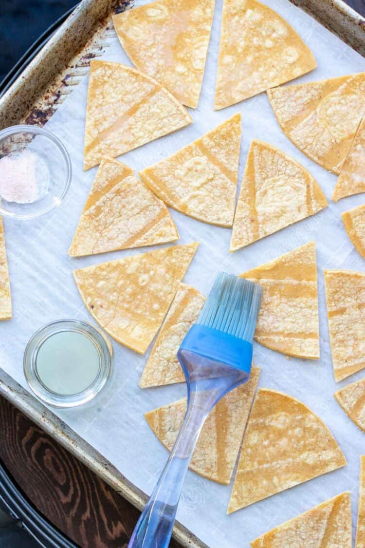 Pastry brush brushing triangles of corn tortillas with lime juice.