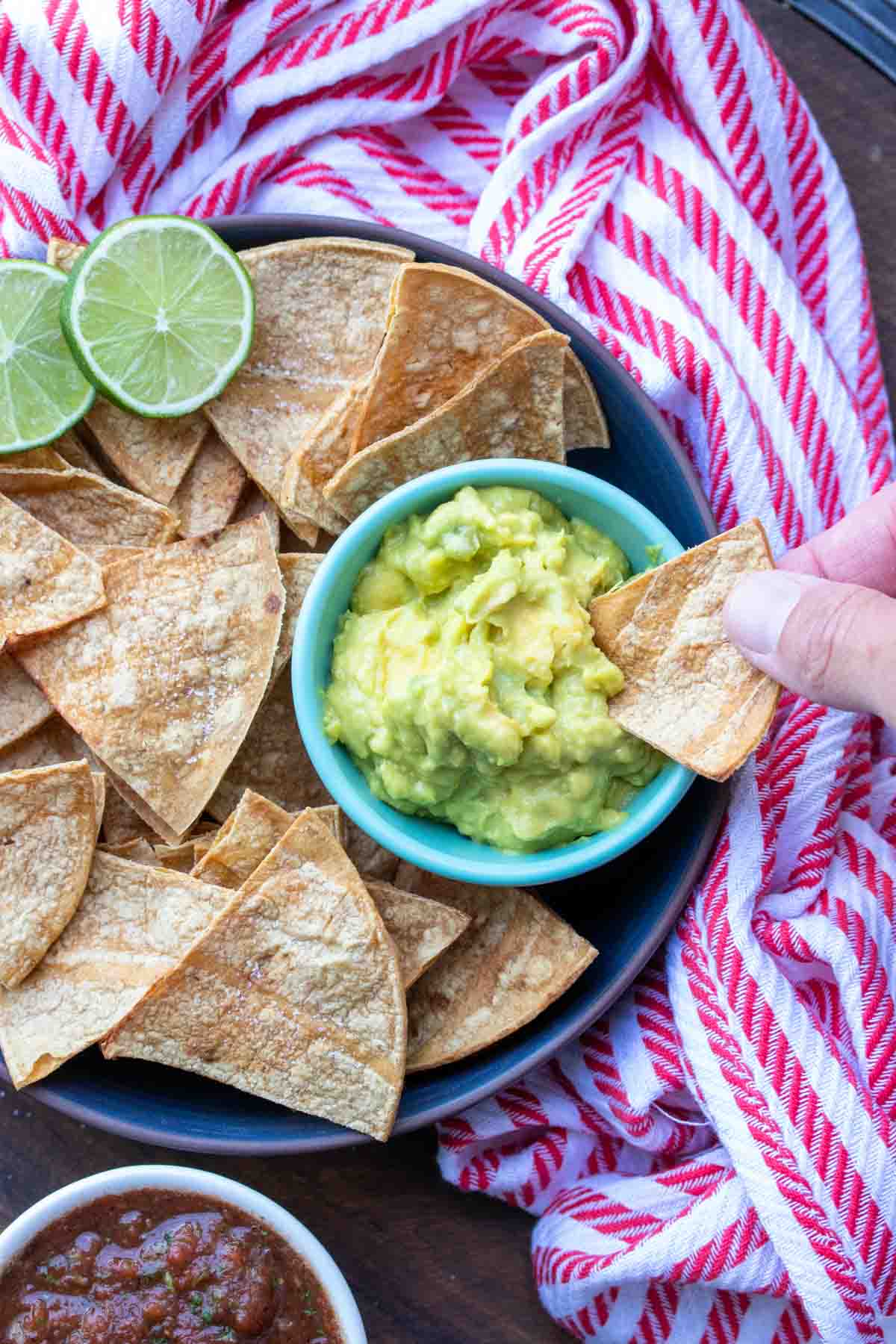 Hand dipping a baked tortilla chip into a small bowl of guacamole.