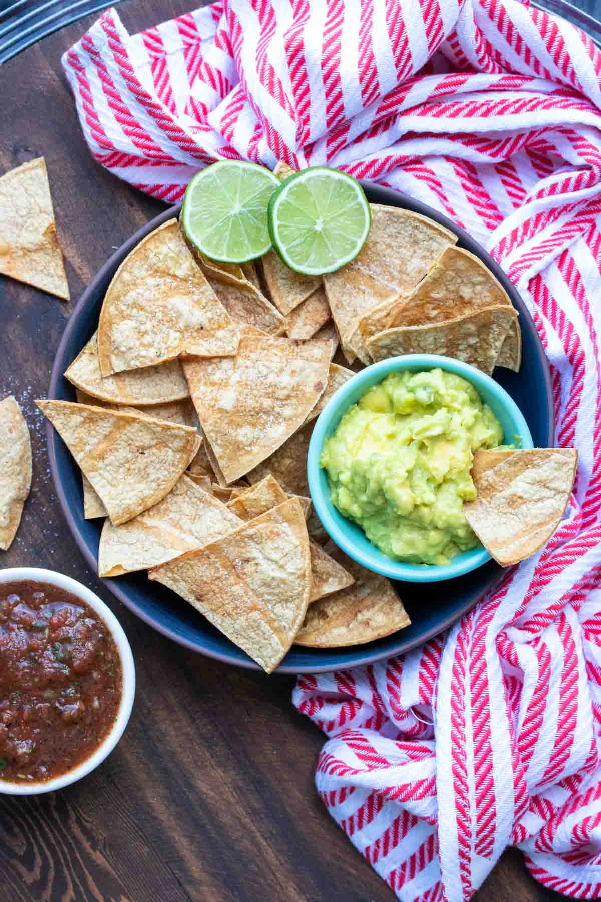 Black plate with baked tortilla chips and small bowl of guacamole.