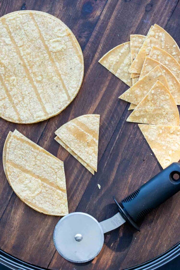 Pizza cutter on a wooden table next to pieces of corn tortillas.